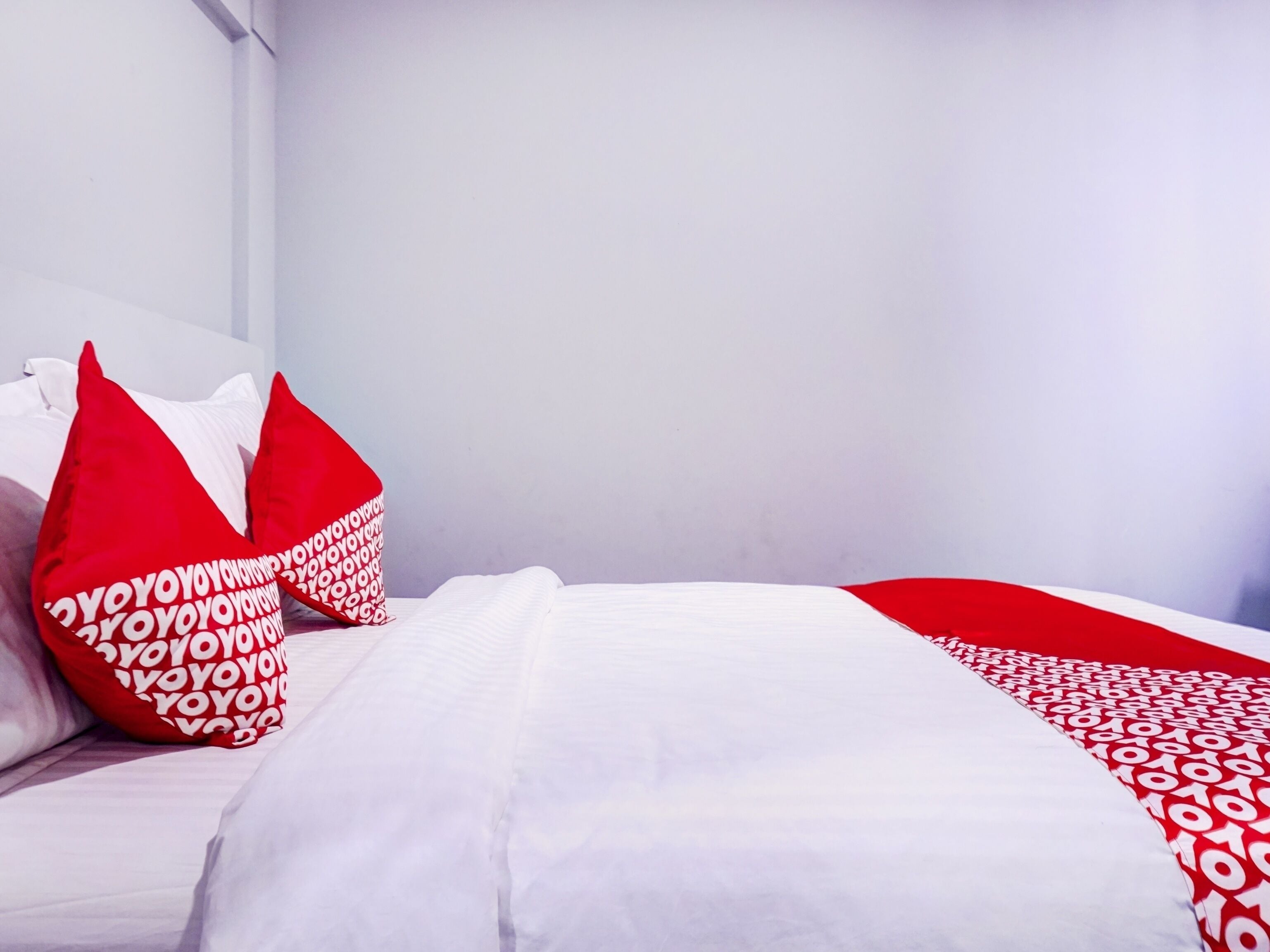 A neatly made bed with white bedding and red pillows with white text.
