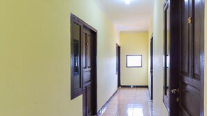 A hallway with yellow walls, dark wooden doors, and a tiled floor. - OYO 2547 Assirot Residence (Jakarta)