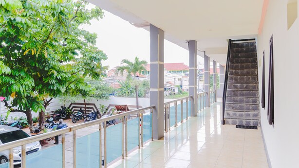 A covered corridor with a staircase, glass railing, and a view of parked motorcycles and cars outside. - OYO 2547 Assirot Residence (Jakarta)