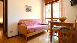 Une pièce confortable avec un lit en bois, une petite table avec des chaises, une fenêtre avec des rideaux et un tableau accroché au mur.