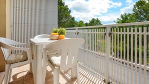 Un balcon avec une table et des chaises blanches, une petite plante en pot et un panier contenant des oranges et une bougie.