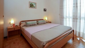 Une chambre à coucher avec un lit en bois, deux tables de chevet avec des lampes, un tableau encadré au mur et une fenêtre avec des rideaux légers.