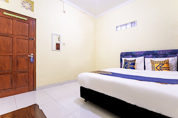 A bedroom with a large wooden door, a bed with patterned pillows, and a small window. - Hotel O Nabila Homestay (Ngaglik)