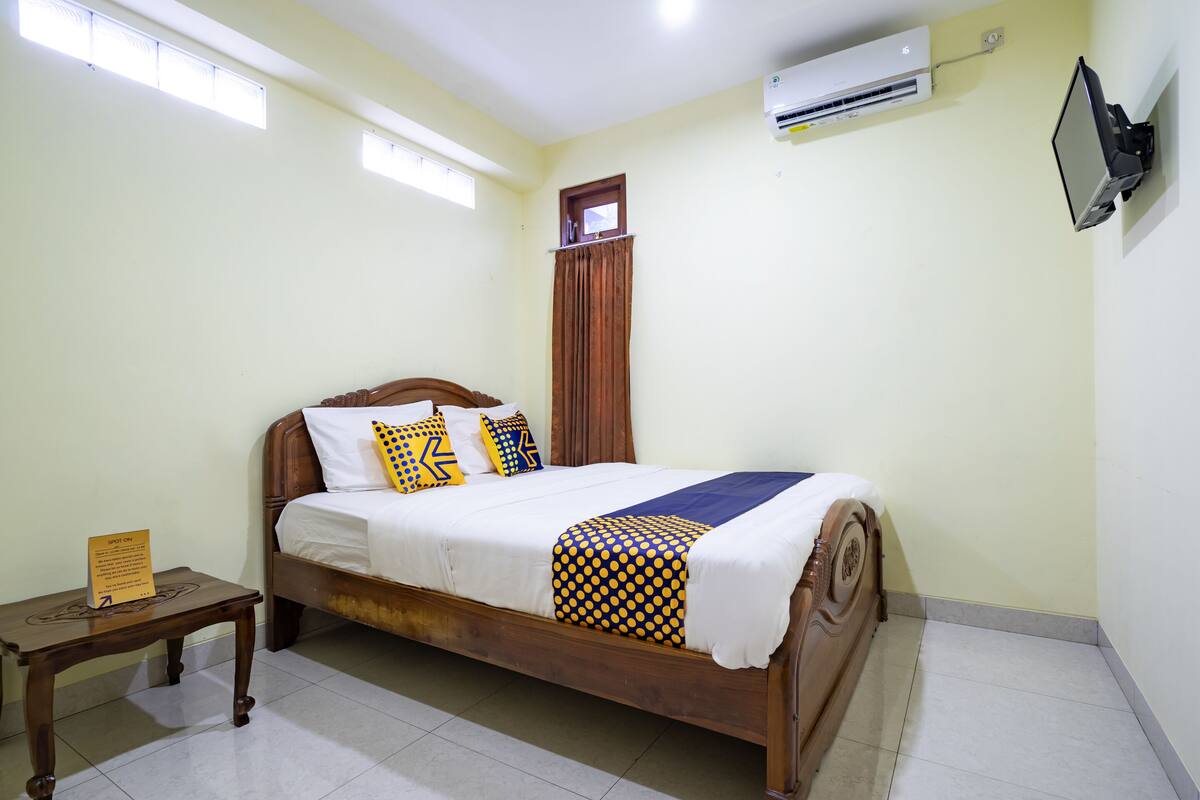 A neatly made bed with a wooden frame, a small bedside table, and a wall-mounted TV.