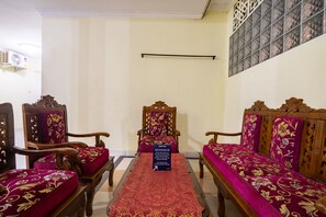 A room with a long wooden sofa set, a matching armchair, and a small table with a red patterned table runner. A sign on the table reads "SPOT ON." - Hotel O Nabila Homestay (Ngaglik)
