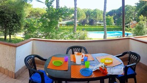 Mesa redonda con sillas en un balcón con vistas a una piscina y vegetación exuberante.