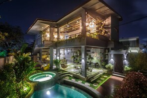 Uma casa de dois andares com piscina, área de estar externa e varanda com plantas.