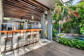 A modern outdoor bar area with a wooden counter, bar stools, and a poolside view.