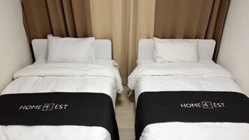 Two twin beds with white bedding and black headboards, each with a 'HOME 4 EST' logo.