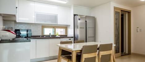 A modern kitchen with white cabinets, a stainless steel refrigerator, and a dining table with chairs.