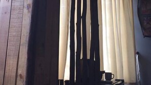 Een kamer met een houten wand, een raam met beige gordijnen en een klein tafeltje met een kop.