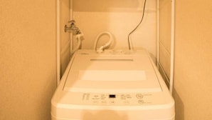 A compact laundry area with a washing machine, a shelf with folded towels, and a basket on top. - SAKIZO VILLA Kyoto Jingu-michi Sanjo 304 (Kyoto)