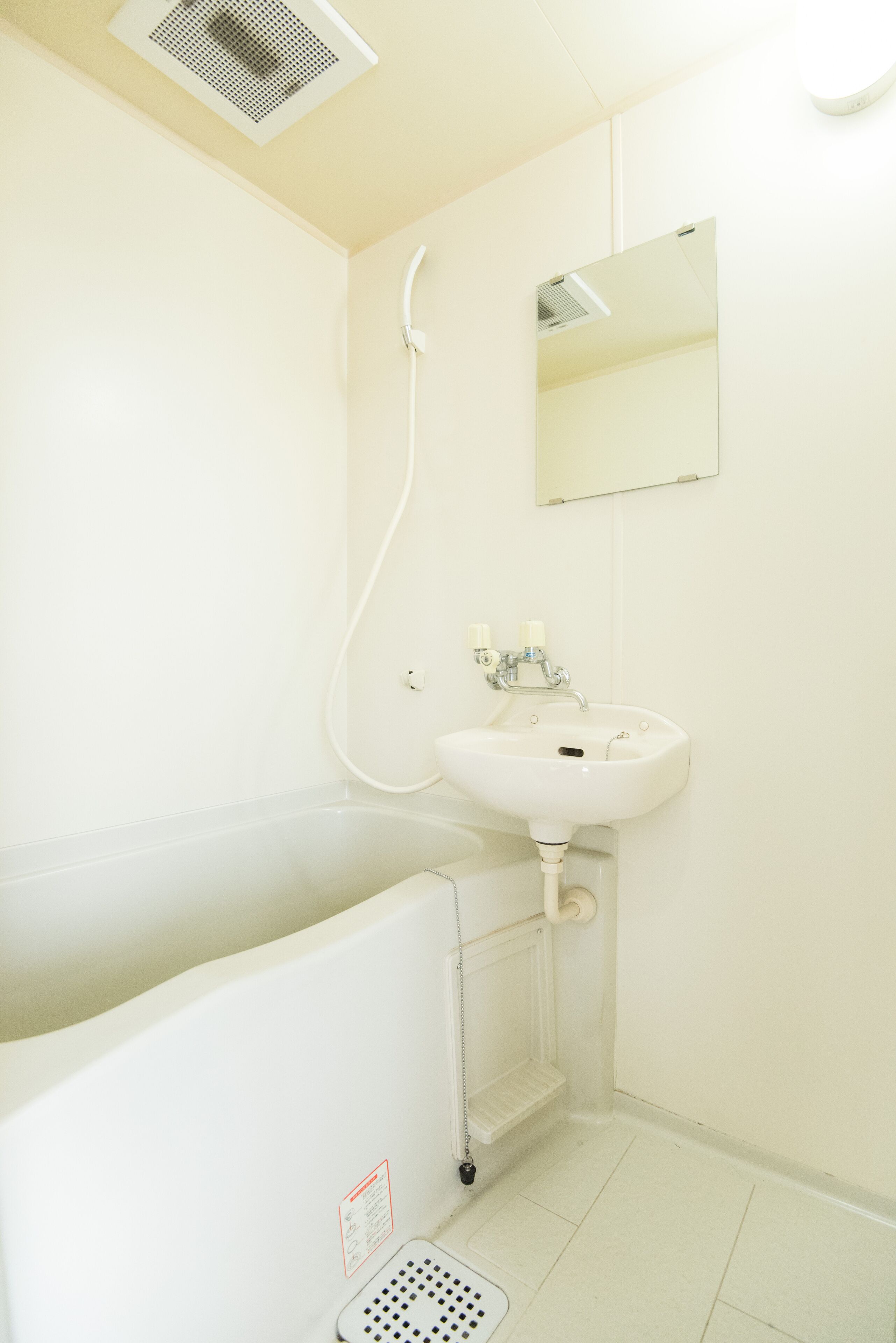 A small, white bathroom with a sink, mirror, and shower.
