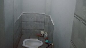 Ein kleines, schmales Badezimmer mit Toilette, einem kleinen Ablagefach für Toilettenartikel und einem Fliesenboden.