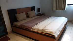 Ein Zimmer mit einem Einzelbett, einem Holzkopfstück, einem Nachttisch mit Lampe und einem Vorhangfenster.