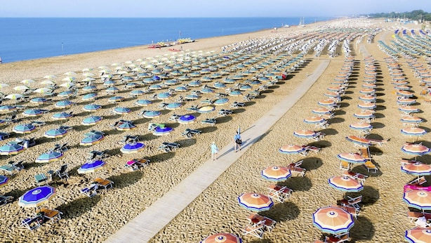 Een strand met rijen parasols en stoelen, een houten looppad en de oceaan op de achtergrond.
