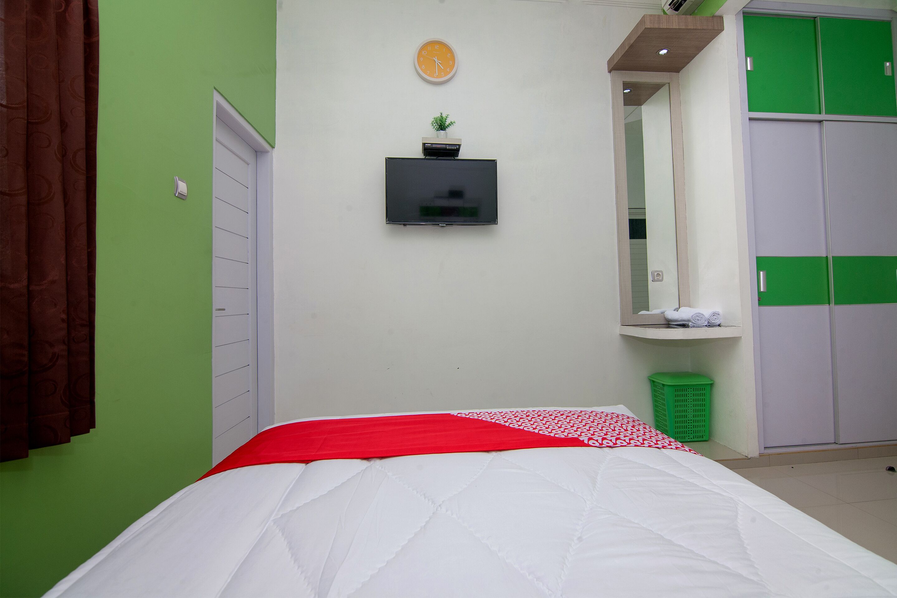 A bedroom with a bed, a television mounted on the wall, a green trash bin, and a wardrobe with green doors.