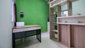 Ein Zimmer mit grüner Wand, einem Holztisch mit einem Laptop, einem weißen Schrank und einem Regal mit Tassen.