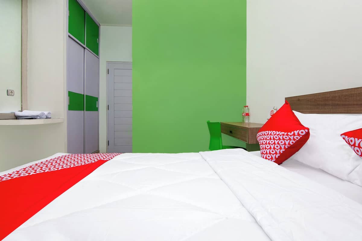 Quarto de hotel com cama, paredes verdes, porta branca e mesa de cabeceira de madeira.