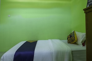 A single bed with a white and blue bedspread, a pillow with a yellow and black pattern, and a green wall.