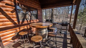 A wooden deck with a round table and bar stools, surrounded by a wooden fence and trees.