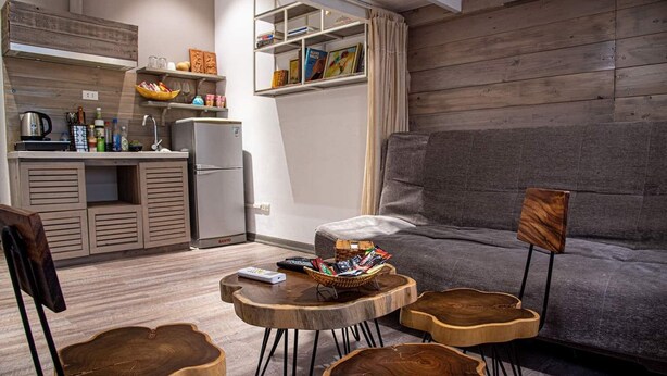 Un espace de vie compact comprenant un coin cuisine, un canapé gris et une table basse avec un panier.