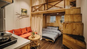 Une chambre confortable, aménagée dans le style d’un chalet, avec un lit en mezzanine, un canapé, une table à manger et un coin cuisine.