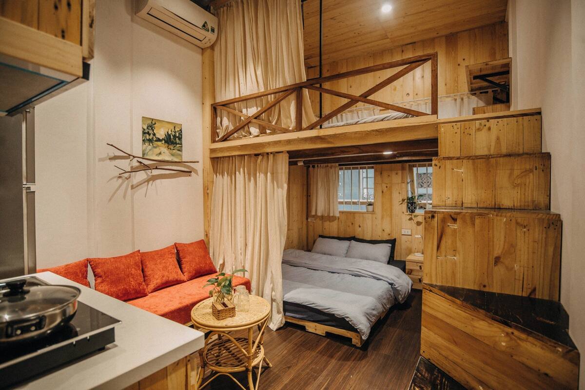 A cozy cabin-style room with a loft bed, a sofa, a dining table, and a kitchen area.