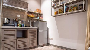 Une cuisine compacte équipée d’un réfrigérateur intégré, d’un évier et d’une étagère où sont rangés des livres et des objets décoratifs.
