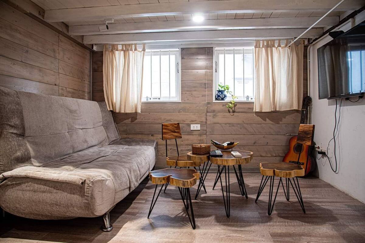 A cozy living room with a sofa, a small round table with chairs, a guitar, and a TV mounted on the wall.