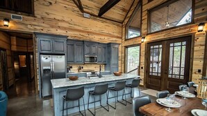 A spacious kitchen with a large island, dark wooden cabinets, and a dining area with a wooden table and chairs. - Across the Universe - Broken Bow/Hochatown- 3bd (Broken Bow)