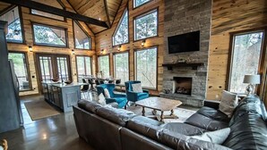 A spacious living area with a large leather sofa, blue chairs, and a stone fireplace. - Across the Universe - Broken Bow/Hochatown- 3bd (Broken Bow)