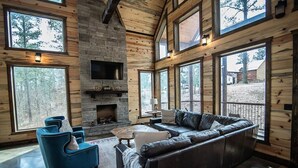 A log cabin interior with a stone fireplace, leather sofa, and large windows. - Across the Universe - Broken Bow/Hochatown- 3bd (Broken Bow)