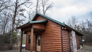 Eine Blockhütte mit Veranda, einem Steinkamin und einem Schotterweg.