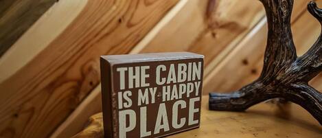 A wooden cabin interior with a sign stating "THE CABIN IS MY HAPPY PLACE."