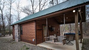Eine rustikale Holzhütte mit Steinunterbau, einer überdachten Veranda mit Sitzgelegenheiten und einem Grillbereich.
