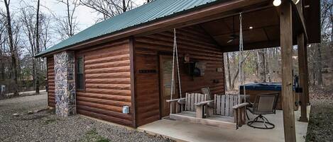 Eine rustikale Holzhütte mit Steinunterbau, einer überdachten Veranda mit Sitzgelegenheiten und einem Grillbereich.