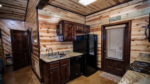 Eine kompakte Küche mit Holzwänden, einer Granitarbeitsplatte, einem Spülbecken, einem Kühlschrank und einem Herd.