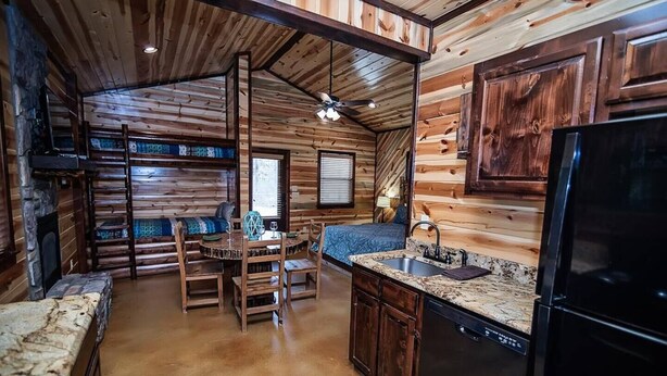Ein gemütliches Blockhaus-Interieur mit einem Holztisch, Stühlen, einer Küchenzeile mit Kühlschrank und einem Kamin.