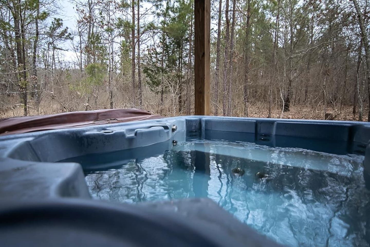 Un bain à remous situé dans un espace boisé, avec une terrasse en bois et une vue sur les arbres environnants.