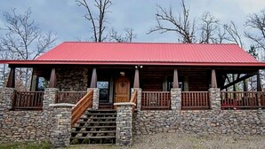 A lodge with a red roof, stone walls, and a wooden staircase leading to a front door. - Lake Ridge Retreat- Broken Bow/Hochatown- 2bd (Broken Bow)