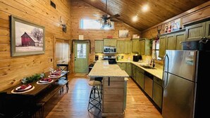 A wooden cabin interior with a kitchen, dining area, and a bar stool. - Lake Ridge Retreat- Broken Bow/Hochatown- 2bd (Broken Bow)