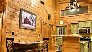 A wooden cabin interior with a dining area, kitchen, and bar. - Lake Ridge Retreat- Broken Bow/Hochatown- 2bd (Broken Bow)