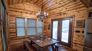 A wooden cabin interior with a dining table set for four, a chandelier, and a 'Welcome to the Cabin' sign. - Moonshine River Retreat- Broken Bow/Hochatown- 2bd (Broken Bow)