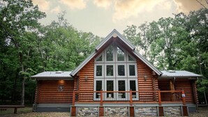 A log cabin with a central chimney, large windows, and a stone foundation. - R-N-R- Broken Bow/Hochatown- 2bd - Sleeps 8 (Broken Bow)