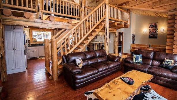 A spacious log cabin interior with a wooden staircase, leather couches, and a rustic dining area. - R-N-R- Broken Bow/Hochatown- 2bd - Sleeps 8 (Broken Bow)
