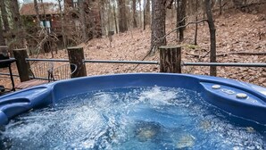 A hot tub in an outdoor setting with a wooden fence and trees in the background. - Seven Eagles- Broken Bow/Hochatown- 2bd (Broken Bow)