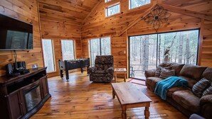 A wooden cabin interior with a television, foosball table, sofa, and a fireplace. - Seven Eagles- Broken Bow/Hochatown- 2bd (Broken Bow)