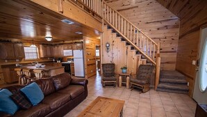 A cabin interior with a wooden staircase, a living room with a sofa and coffee table, and a kitchen area.