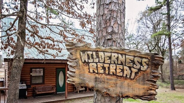 A rustic wooden sign reading "WILDERNESS RETREAT" attached to a tree.
